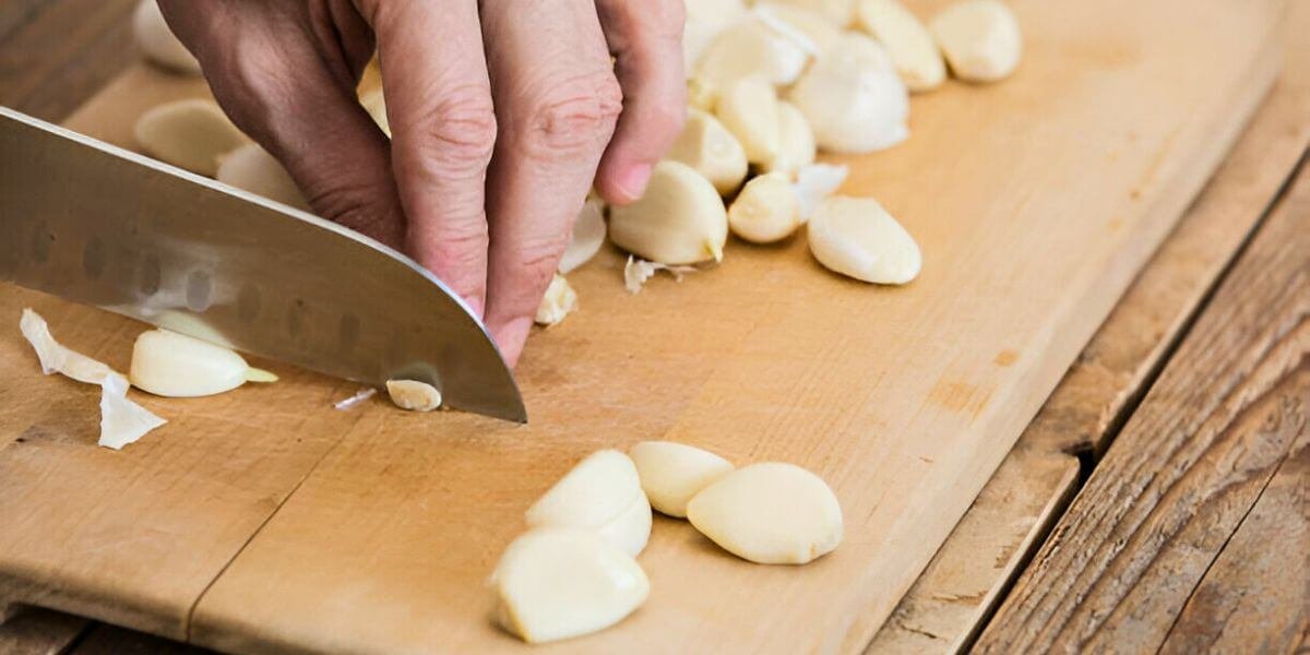 Close-up of hands chopping garlic with a Santoku knife on a wooden cutting board