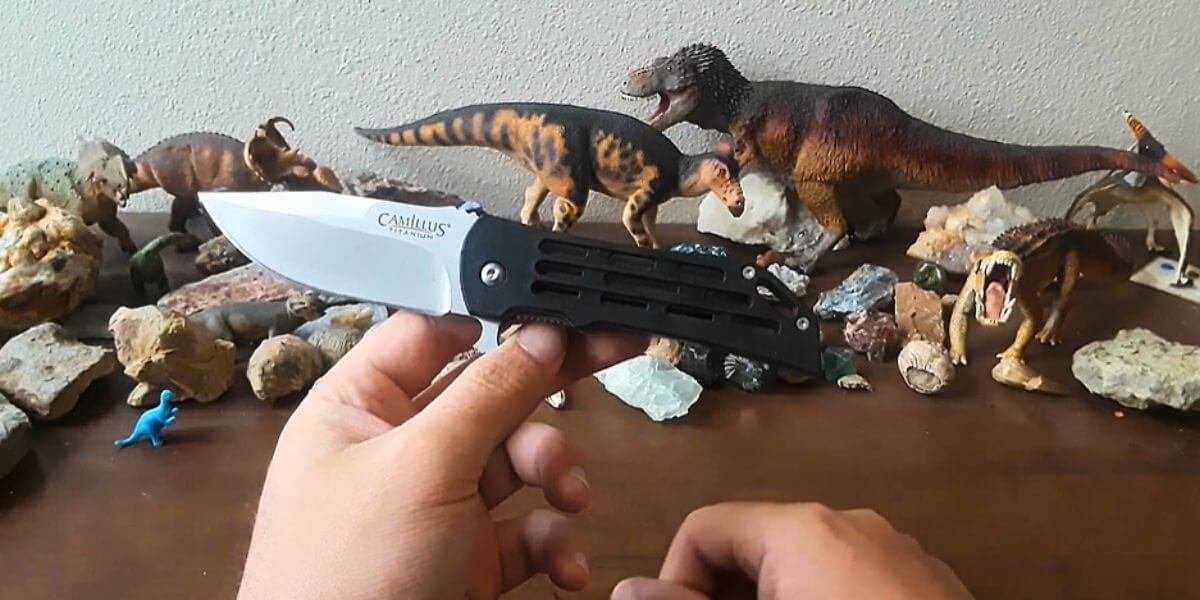 Person holding a Camillus Titanium knife with dinosaur figurines in the background.