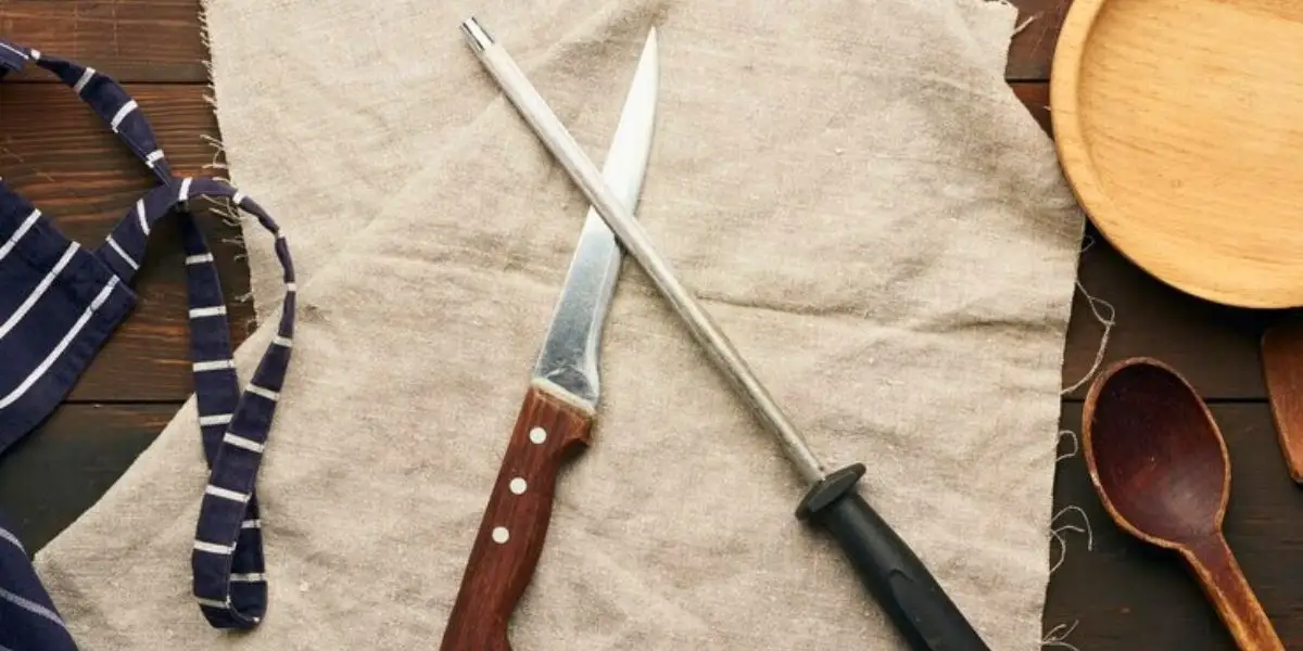 Boning knife and honing steel placed on a rustic kitchen setup with wooden spoons and an apron