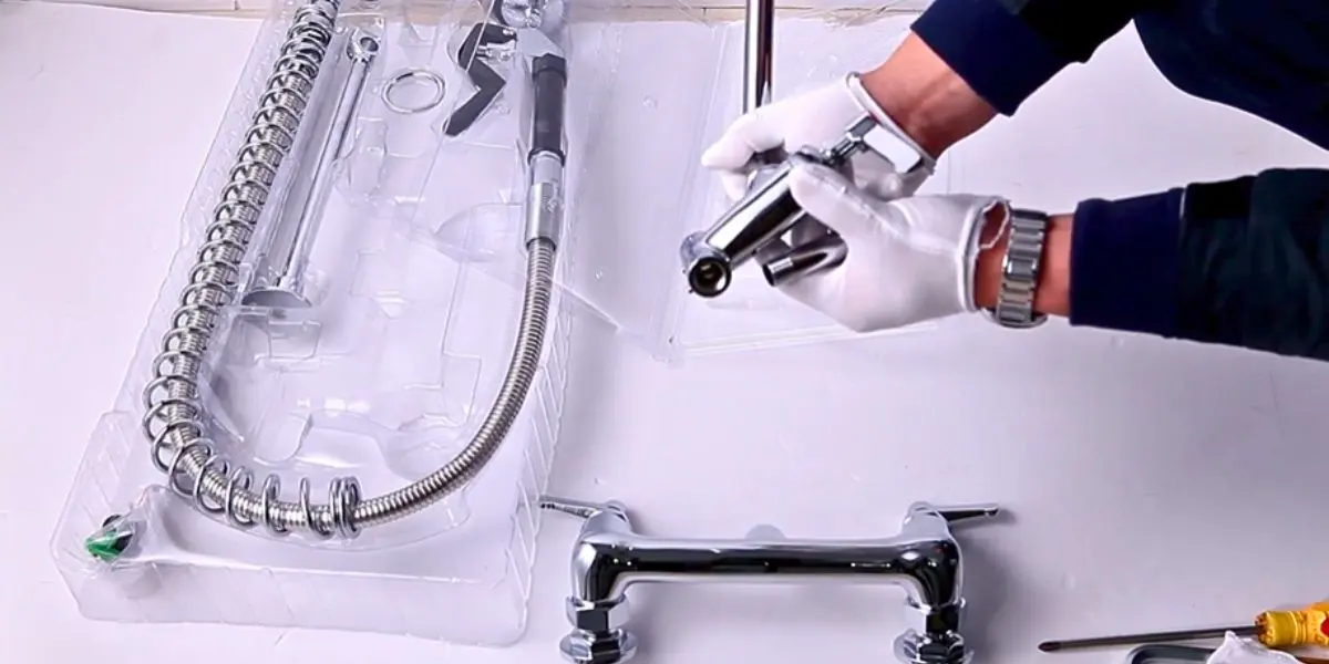 A man wearing gloves installs a kitchen sink sprayer